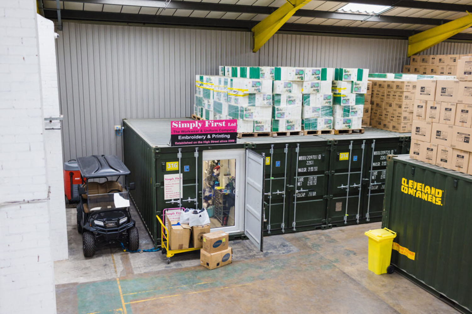 Green storage container used by a printing business, with pallets of stock stacked above