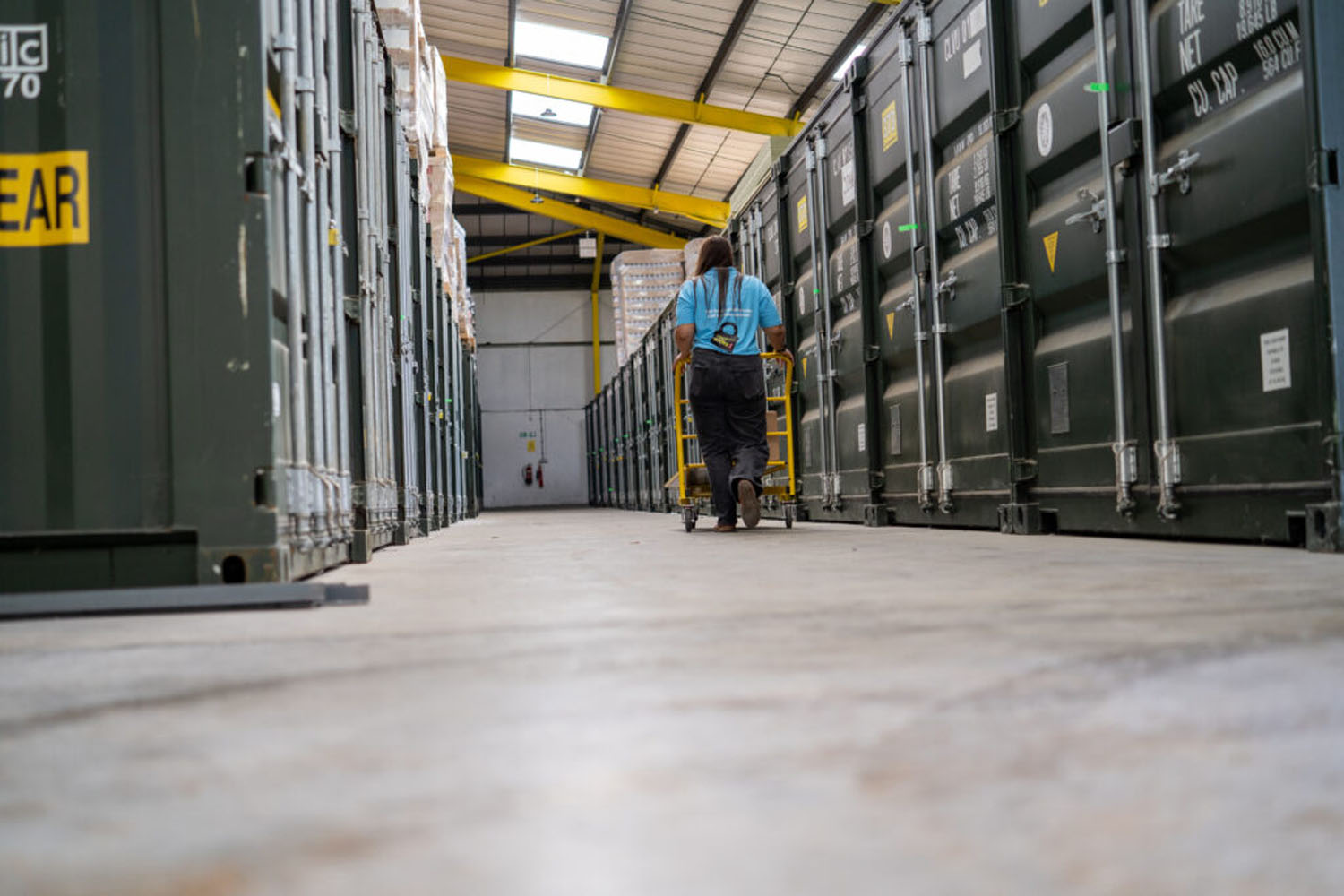 Staff member wheeling a trolley along an aisle of green storage containers