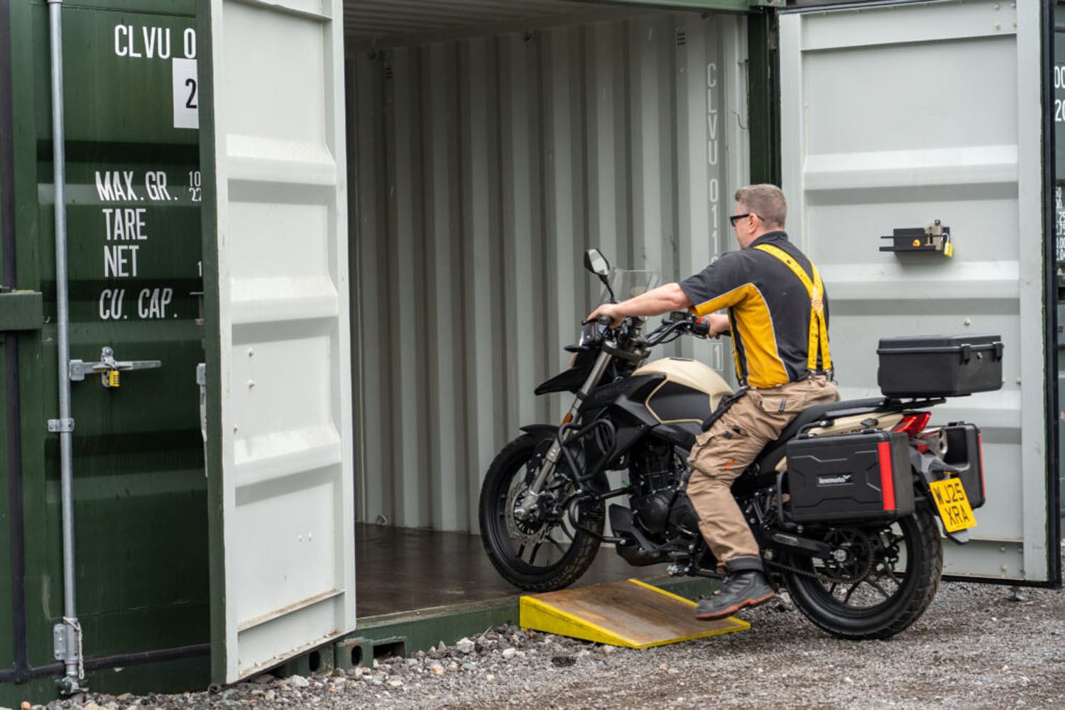 Customer wheeling a motorbike into a green storage container up a loading ramp