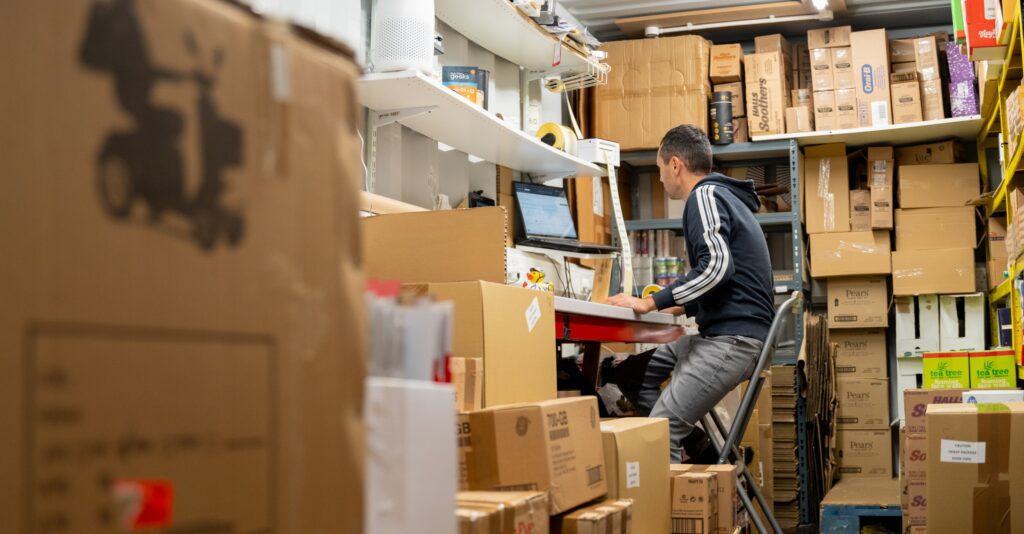 Online retailer packing orders at a desk surrounded by stock in a business pod