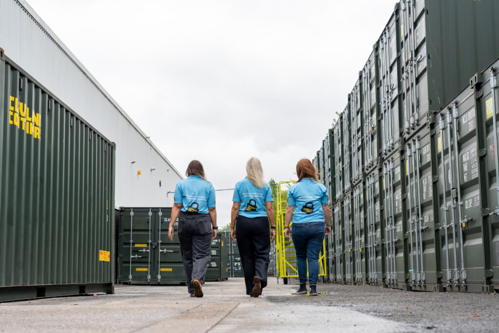 Three team members walking between rows of green storage containers