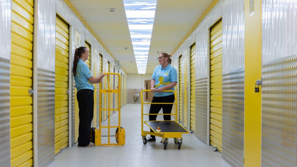 Team members with trolleys in a corridor of yellow indoor storage units